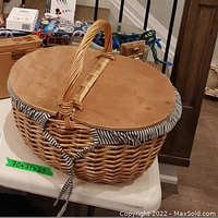 Closed woven picnic basket with wooden lid and handle, sitting on white surface.