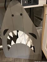 Large wooden cut-out shark artwork in gray and white with stylized open mouth and eyes