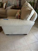 Side view of cream fabric armchair with floral pillow on seat.