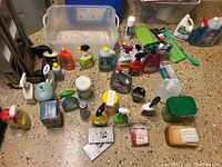 Overall view of assorted cleaning products arranged on floor with clear plastic bin behind