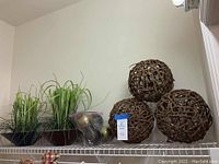 Photo showing three woven wicker spheres in different sizes and two faux grass plants in a brown container with small metallic balls.