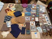 Overview photo showing the mix of dish towels, trivets, napkin rings, placemats, coasters, wine bottle stoppers, and mini mirrors laid out on a bed.