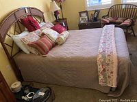 Full side view of the dressed bed showing mattress, bedspread, pillows, headboard, and part of room