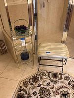 Full view of brass three tier shelf with glass shelves and metal bench with padded seat beside it, rug partially visible in foreground