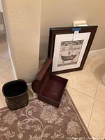 Framed bathroom wall decor, small treasure chest open, and decorative waste can on floor