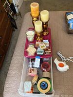 Candle trio on wooden holders, assorted wax melts in plastic containers, jasmine scented candle, and white ceramic dove-shaped warmer with cord on bed