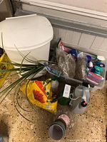 Overview photo showing bags of potting soil, garden chemicals, sprayer, gloves, small pots, and other gardening supplies in a garage setting on a tile floor.