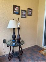Metal occasional table with glass top and two matching lamps displayed on lanai corner under three small floral wall decor pieces.