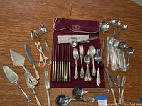 Full view of flatware pieces arranged on dining table, including knives, forks, spoons, and serving utensils along with storage case.