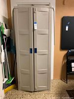 Closed front view of the Suncast utility storage cabinet showing the two doors and blue handles on a beige wall background.