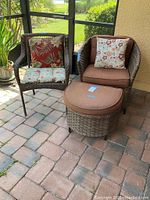 Wicker armchair with brown cushions and floral pillow, side chair with floral cushions, and ottoman on brick patio