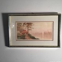 Full view of the framed watercolor painting showing the cabin, trees, water, and opposite shore in a misty environment. The frame is gold colored with visible slight wear on edges.