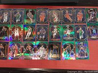 Image showing 21 assorted basketball rookie trading cards with holographic effects featuring NBA players in action poses, arranged in three rows on a red background.