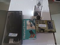 Photo of the lot showing heated gloves, heated socks box, 12MP trail camera box, and smart watch with manual