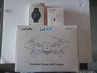 Photo of lot with Zuhafa foldable drone box, smart bracelet box, and Bottun wireless earbuds box against white background.