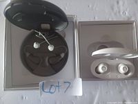 Top-down photo showing two pairs of wireless earbuds with their respective charging cases—one white set and one black set with ear hooks.
