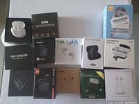 Image showing 12 boxes and charging cases of various true wireless earbuds in black and white packaging with multiple brands