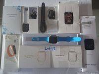 Top view showing six smart watches, multiple accompanying boxes, charging cables, and one bright blue wristband watch on display