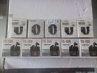 Photo showing five boxed Lestar TS100 fitness trackers and five boxed TS-100 wireless earbuds arranged in two rows on a white background.