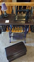 Full view of the antique Davis sewing machine mounted on a wooden table with cast iron treadle base, small lamp, and wooden cover.