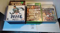 Photo of 16 video games stacked in two rows showing NHL 2001 (PC), Grand Theft Auto IV (Xbox), and a PlayStation game with visible cases and artwork.