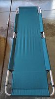 Green camping cot with fabric stretched on metal frame shown on concrete floor