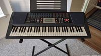 Front view of Casio CTK-501 keyboard on stand, showing keys, speakers, and control panel with display and buttons.