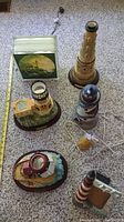 Overview of six lighthouse-themed items including electric lighthouses, a picture frame, beeswax candle, and tea light holder on carpet.