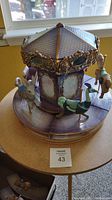 Full view of the hand made ceramic carousel with animal figures on wooden base and stand placed on a small table.