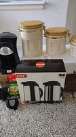 Photo showcasing three ceramic canisters with wooden lids, boxed thermal carafes set by Copco, and part of the Proctor Silex coffee maker setup