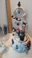 Full view of penguin-themed clock with multiple figurines around and on it, showing scale with a ruler nearby