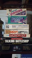 Stack of board games including Yahtzee (Mickey Mouse edition), Boggle Master, 500-piece puzzle box, Sorry! and Monopoly combined box, and Electronic Talking Battleship large box.