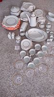 Full arrangement of the Noritake Gloria and Celebrity Duet China set on carpet showing plates, cups, serving dishes, and water glasses with gold rims.