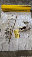 Overview of two gardening augers, instructions, and original box laid out on white towel.