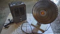 White circular parabolic Presto HeatDish Plus electric heater with metal grill, plastic base, and power cord visible on towel on concrete floor