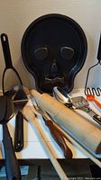 Photo showing skull cake pan and various kitchen utensils including rolling pins, Cutco fork, Zylco spoon, and other cooking tools.