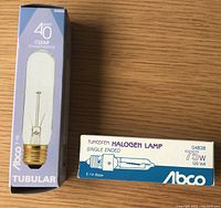 Photo showing two Abco appliance bulbs with boxes: one 40 watt clear tubular bulb and one 75 watt tungsten halogen bulb labeled with specifications.