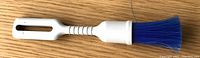 Top view of the clean-up brush showing white plastic handle with opening for hanging, flexible neck, and blue bristles.