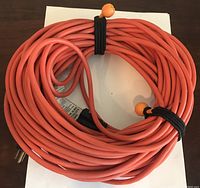 Coiled orange electrical extension cord with 3-prong plug ends, secured with cable ties.