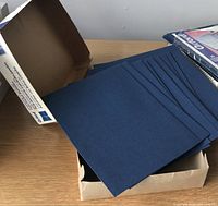 Nine blue twin pocket folders stacked inside an open cardboard box, showing their flat front covers in good condition.