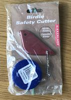 Birdie Safety Cutter and small tape measure in original plastic packaging, cutter is maroon and bird-shaped with ceramic blade indicated on packaging, brand Kikkerland present.