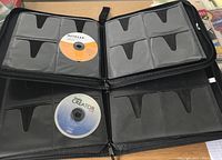 Open view of the two black disc storage notebooks showing clear sleeves with slots for CDs/DVDs, one smaller and one larger notebook each with labeled discs inside.