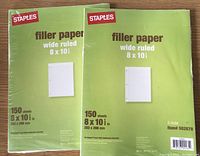 Two unopened packs of green Staples wide ruled filler paper, each pack has 150 sheets measuring 8 x 10.5 inches and punched for 3-ring binder.