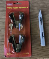 Photo shows two claw staple removers in sealed Staples packaging along with one white Swingline nipper staple remover placed beside the package.