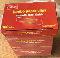 Photo of stacked red boxes labeled Staples jumbo paper clips with 100 clips per box, smooth steel finish, item #525923.