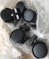 Photo shows five black plastic office chair casters with metal stems and mounting brackets placed inside a clear plastic bag.