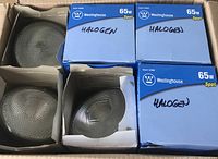 Six 65 watt halogen floodlights in original Westinghouse blue boxes, labeled 'HALOGEN' in marker. Four floodlights partially visible with textured glass lenses.