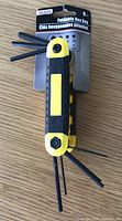 Yellow and black foldable hex key tool with 8 fold-out hex keys shown on a wood surface with original packaging behind.
