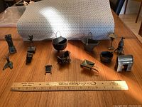 Photo showing 13 miniature steel and cast iron pieces laid out with ruler for scale.