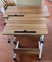 Two rolling TV tables aligned, showing tops and adjustable steel leg frames with wheels